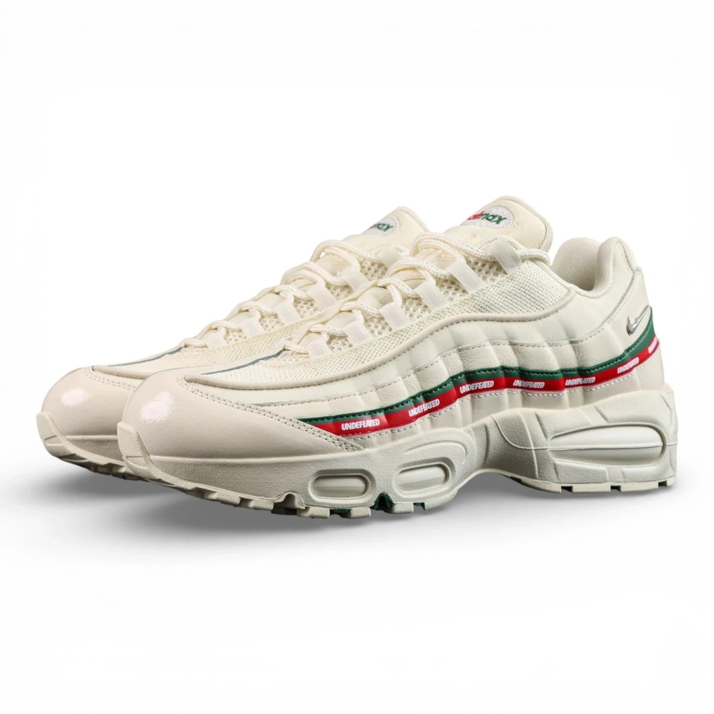 Undefeated x Air Max 95 Sail 2025 - Full Lateral Profile View with White Shoebox on Dark Background Showing Sail Off-White AM95 Upper Dark Green Leather Spine Stripe Red UNDEFEATED Repeat-Text Ribbon and Sail Outsole with Dark Green Square-Block Traction