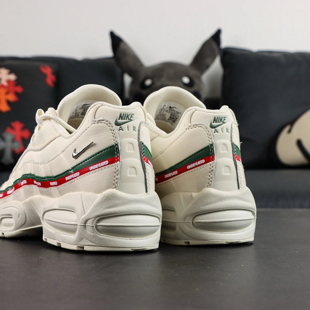 Undefeated x Air Max 95 Sail 2025 - Full Lateral Profile View with White Shoebox on Dark Background Showing Complete Sail Off-White AM95 Upper Dark Green Leather Spine Overlay Stripe Red UNDEFEATED Ribbon and Sail Midsole