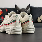 Undefeated x Air Max 95 Sail 2025 - Full Lateral Profile View with White Shoebox on Dark Background Showing Complete Sail Off-White AM95 Upper Dark Green Leather Spine Overlay Stripe Red UNDEFEATED Ribbon and Sail Midsole
