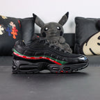 Undefeated x Air Max 95 Black 2025 - Rear Heel View of Both Shoes with Pikachu Plush on Dark Background Showing Red NIKE AIR Text and Red Swoosh Logo on Black Heel Counter Dark Green Leather Spine Stripe and Red UNDEFEATED Ribbon