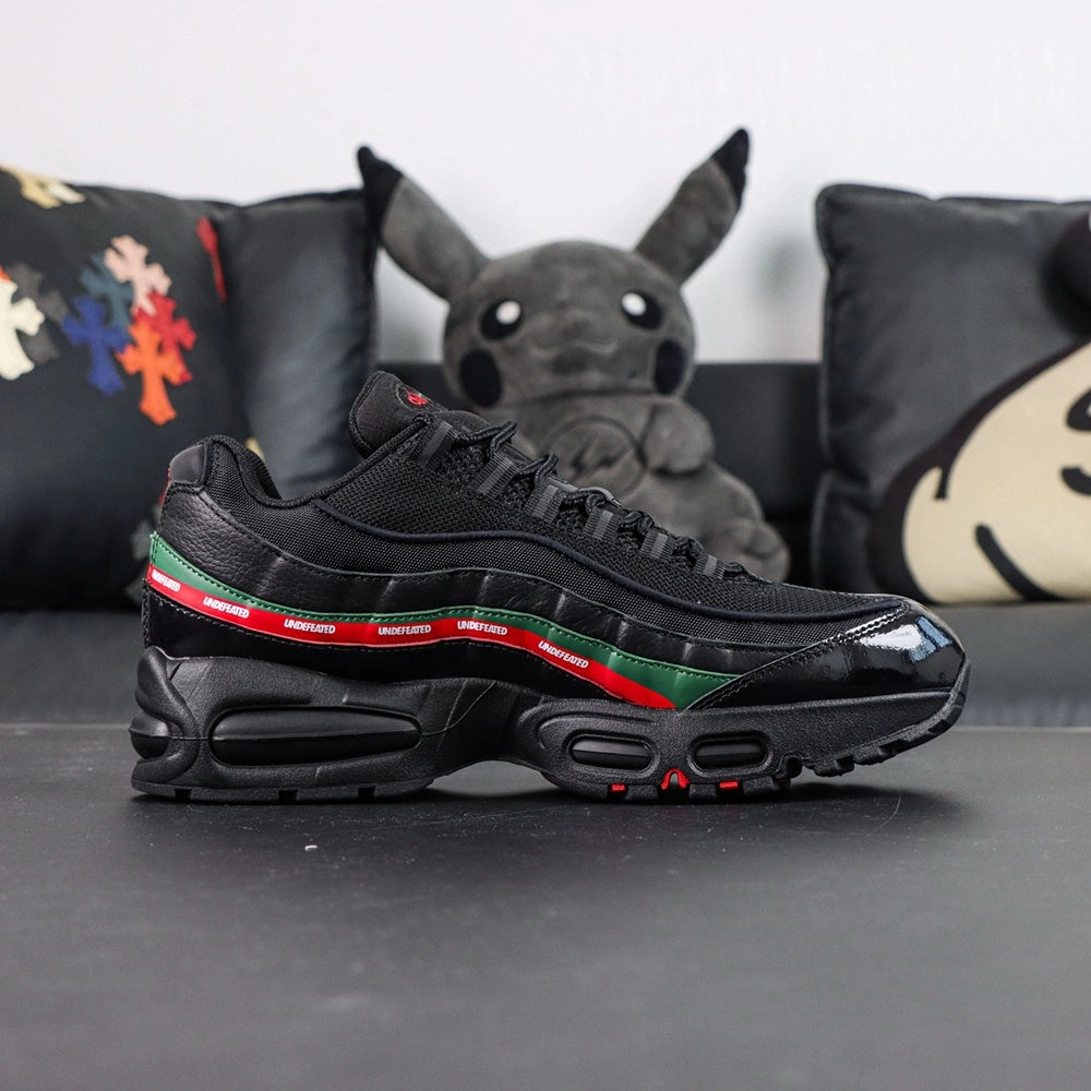 Undefeated x Air Max 95 Black 2025 - Rear Heel View of Both Shoes with Pikachu Plush on Dark Background Showing Red NIKE AIR Text and Red Swoosh Logo on Black Heel Counter Dark Green Leather Spine Stripe and Red UNDEFEATED Ribbon