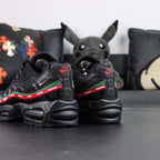 Undefeated x Air Max 95 Black 2025 - Tongue and Ankle Collar Top Down View on Dark Background Showing Black Air Max Oval Badge with Red Air and Green Max Text Black Undefeated Five-Strike Logo on Tongue Interior and Red Textile Ankle Collar Lining
