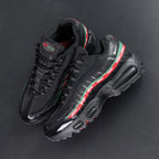 Undefeated x Air Max 95 Black 2025 - Full Lateral Profile View with White Shoebox on Dark Background Showing Complete Triple Black AM95 Upper Dark Green and Red UNDEFEATED Dual Stripe White Mini Swoosh and Black Midsole with Red Accent Edge