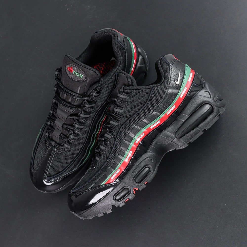 Undefeated x Air Max 95 Black 2025 - Full Lateral Profile View with White Shoebox on Dark Background Showing Complete Triple Black AM95 Upper Dark Green and Red UNDEFEATED Dual Stripe White Mini Swoosh and Black Midsole with Red Accent Edge