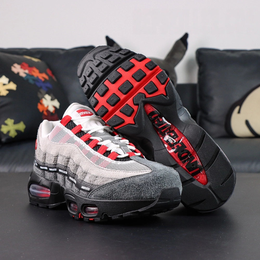 Undefeated x Air Max 95 Bright Crimson 2025 - Full Lateral Profile View with Pikachu Plush on Dark Background Showing White Mesh Light to Dark Grey Suede AM95 Upper Full UNDEFEATED Black Ribbon Typography Grid and Black Midsole with Crimson Air Units