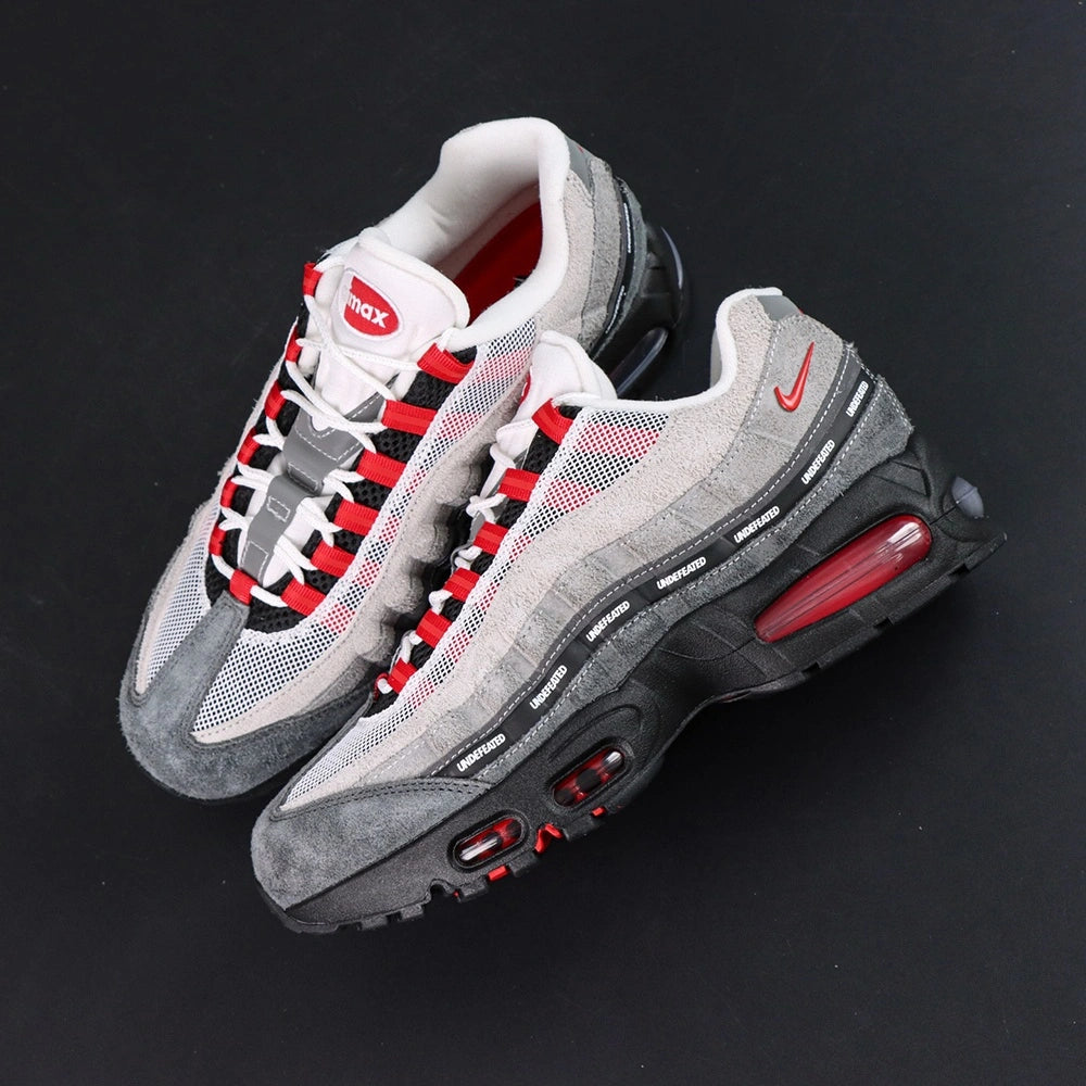 Undefeated x Air Max 95 Bright Crimson 2025 - Rear Heel View of Both Shoes with Pikachu Plush on Dark Background Showing Red NIKE AIR Two-Line Text on Grey Suede Heel Counter Red Mini Swoosh and Crimson Tinted AM95 Air Units in Black Midsole