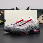Undefeated x Air Max 95 Bright Crimson 2025 - Rear Heel View of Both Shoes on Dark Background Showing Red NIKE AIR Heel Counter Branding Red Mini Swoosh on Lateral Heel and Crimson AM95 Air Units Visible Through Black Midsole Windows