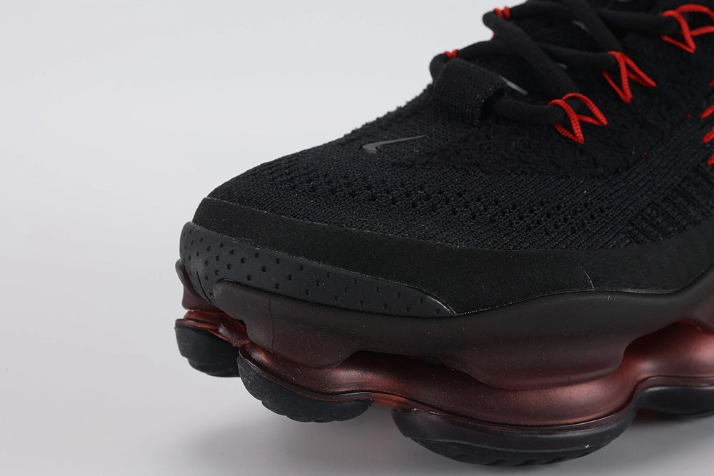 Air Max Scorpion Flyknit Bred Black University Red - Tongue and Lace Area Close Up on White Background Showing Crimson Dot-Grid Tongue Badge Red Oval Lace Locks University Red Paracord Lace Red Accent Stitching Lines on Black Loop-Pile Flyknit and Black Coarse Flyknit Upper