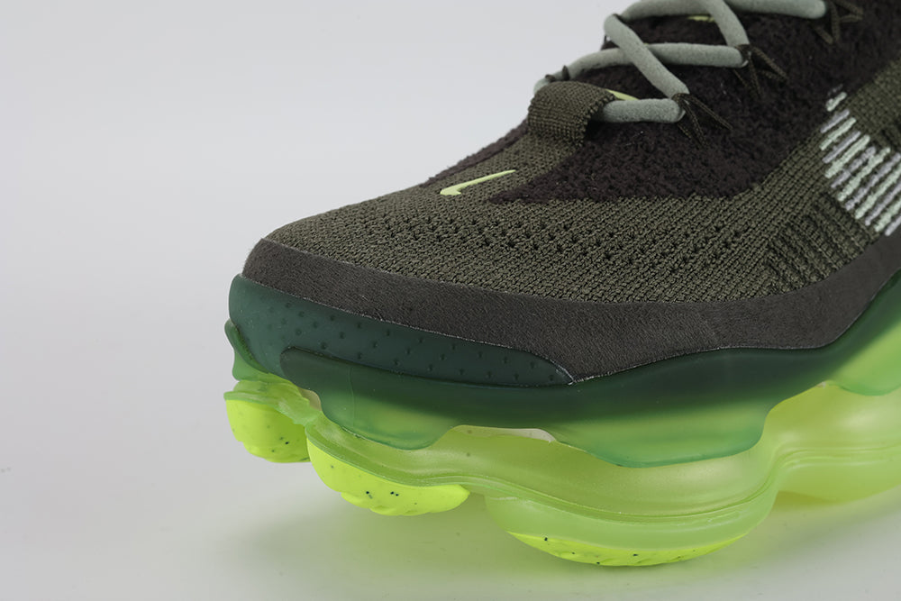 Air Max Scorpion Flyknit Cargo Khaki Volt - Lace Area Close Up on White Background Showing Black X-Form Lace Locks Grey Flat Laces Volt Oval Lace Keeper with White Dot-Grid Texture Volt Oval Tongue Badge Cargo Khaki Loop-Pile Flyknit Upper and White Horizontal Stripe Bands on Lateral Panel
