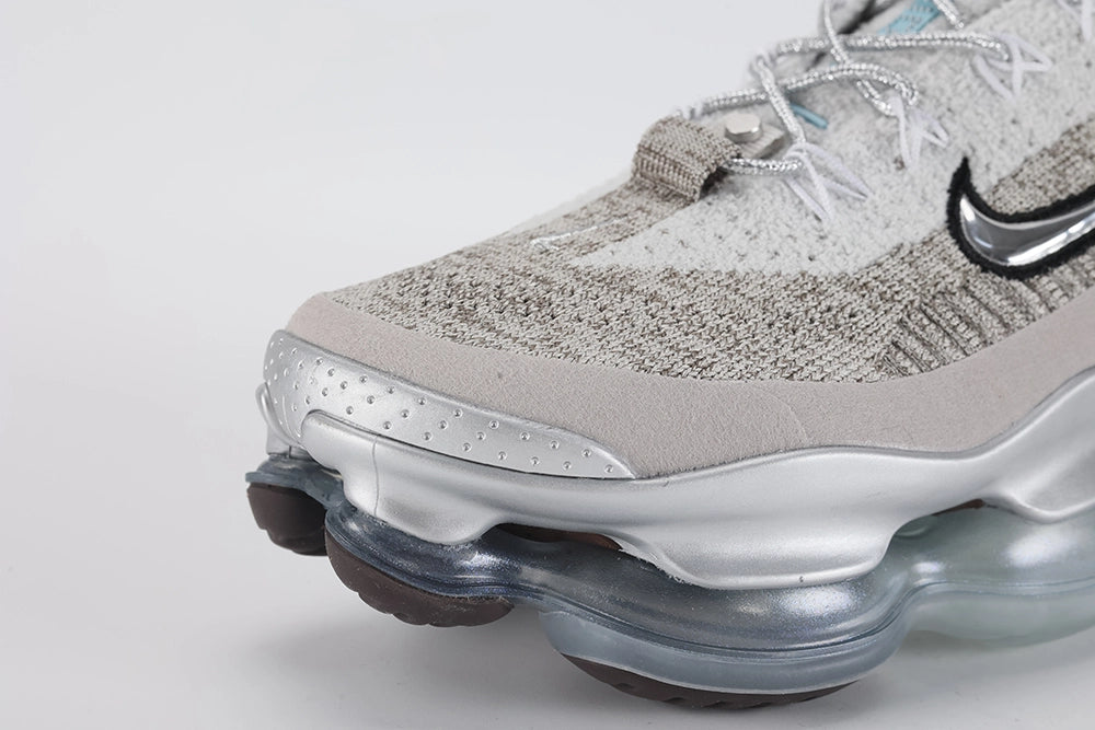 Air Max Scorpion Flyknit Gaiter Light Bone Metallic Silver - Heel Counter Close Up on Grey Background Showing Integrated Smoky Mauve Terry Cloth Gaiter Covering Full Heel Collar Powder Blue Perforated Rectangular Badge at Gaiter Top and Metallic Silver AM Scorpion Air Unit at Heel