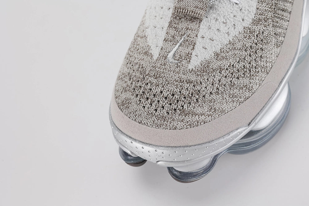 Air Max Scorpion Flyknit Gaiter Light Bone Metallic Silver - Lace Area and Lateral Midfoot Close Up on Grey Background Showing Powder Blue Perforated Rectangular Lace Garage Silver Metallic Rope Lace with Silver Metal Lace Dubrae Black Filled Swoosh Embroidery and Heathered Flyknit Upper