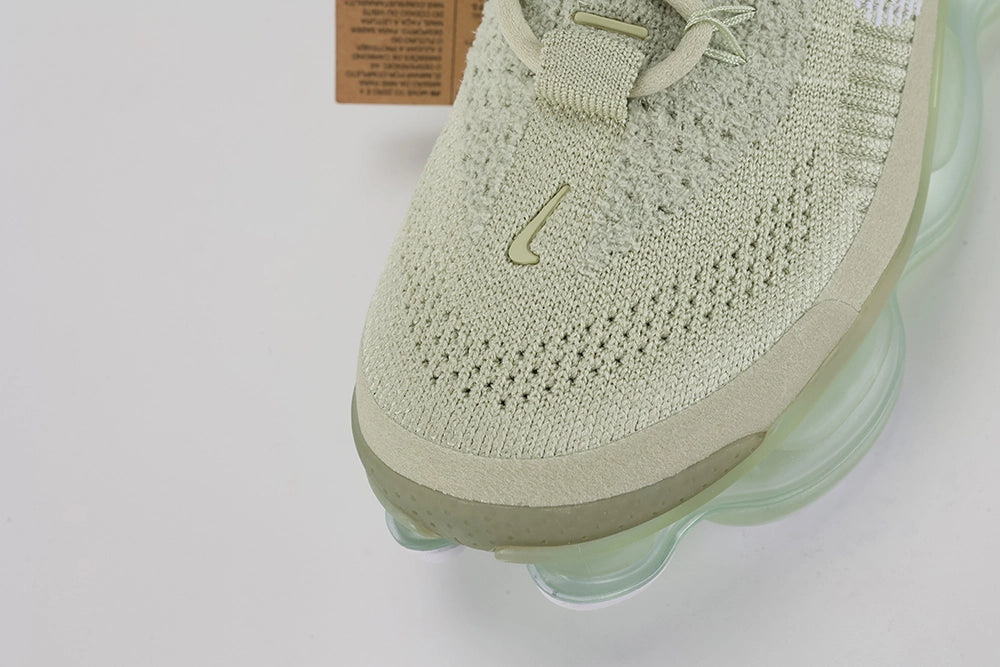 Air Max Scorpion Flyknit Olive Aura Light Bone Sea Glass Volt - Lace Area Close Up on Grey Background Showing Two Light Bone Rectangular Lace Keepers with White Dot-Grid Texture Tan Leather Lace Garage Light Bone Rope Laces White Sketch-Outline Swoosh on Lateral Midfoot Boucle Flyknit with Silver Metallic Thread and Sea Glass AM Scorpion Air Unit