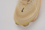 Air Max Scorpion Flyknit Sesame Dark Driftwood Total Orange - Rear View of Both Shoes on White Background Showing Sesame Wide Rubber Heel Pull Tabs with Dark Driftwood Dot-Grid Texture Sesame Collar Lining Tan Kraft Paper Hang Tags and Lemon Chiffon to Total Orange Gradient AM Scorpion Air Unit at Heel with Orange Chambers Visible