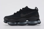 Air Max Scorpion Flyknit Triple Black Anthracite - Toe Box Close Up on Grey Background Showing Black Fine-Knit Flyknit Toe Box Anthracite Mini Swoosh Embroidery Black Perforated Suede Overlay at Lower Zone with Dense Small-Circle Perforation Pattern and Black AM Scorpion Air Unit at Forefoot