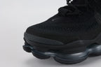 Air Max Scorpion Flyknit Triple Black Anthracite - Lace Area and Lateral Midfoot Close Up on Grey Background Showing Black Iridescent Flyknit on Lateral Midfoot Upper Zone Shifting to Deep Blue Green Purple Under Light Black Perforated Suede Overlay at Lower Zone Black Rectangular Lace Keeper with Dot-Grid Texture Black Rope Laces and Black to Dark Smoke Grey AM Scorpion Air Unit