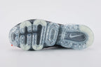 Air VaporMax co-branded Part 2 Black White Orange - Heel Counter Close Up on White Background Showing Black Woven Heel Pull Tab with Orange Rectangular Accent at Top White AIR Quotation-Mark Text at Heel Midsole Junction VAPORMAX Text on Heel Collar White Co-Branded Text System at Heel Counter and Frosted Ice VaporMax Air Unit at Heel