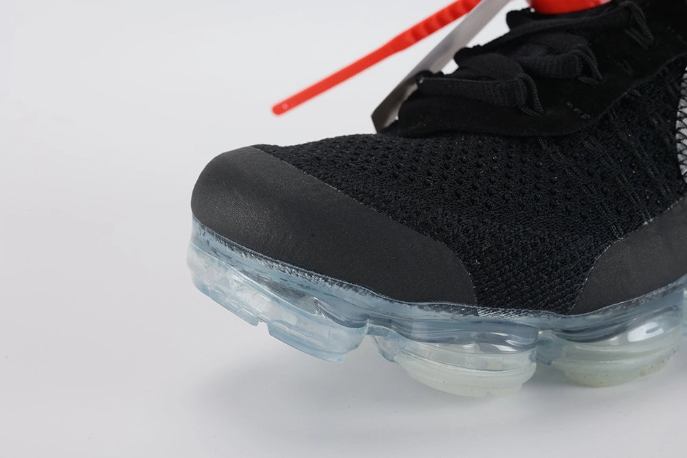 Air VaporMax co-branded Part 2 Black White Orange - Tongue and Lace Area Close Up on White Background Showing White Rectangular Woven Tongue Label with Black Co-Branded Sportswear Text and Orange Swoosh Orange Industrial Zip Tie with Serrated Edge Transparent Circular Plastic Hang Tag Black Rope Laces and Black Fine-Knit Flyknit Upper