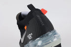 Air VaporMax co-branded Part 2 Black White Orange - Rear View of Both Shoes on White Background Showing Black Woven Heel Pull Tabs with Orange Rectangular Accent White AIR Quotation-Mark Text at Heel Midsole Junction White Co-Branded Text System at Heel Counter Orange Industrial Zip Tie and Frosted Ice VaporMax Air Unit at Heel